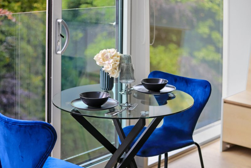 Dining table with blue chairs, place settings, flowers and water glass by large window