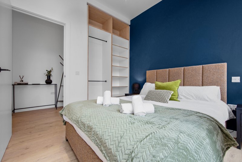 Modern bedroom with double bed, upholstered headboard, blue accent wall and wooden wardrobe