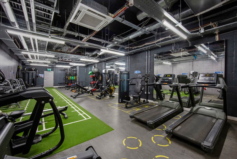 Modern gym interior with exercise equipment, bright green floor markings, industrial ceiling and fluorescent lighting