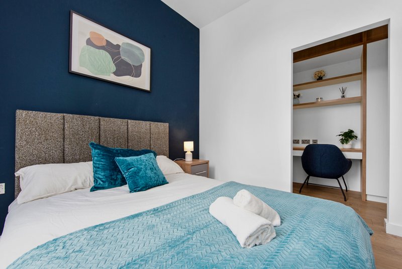 Modern bedroom with double bed, blue bedding, teal cushions, dark blue accent wall, and built-in shelving