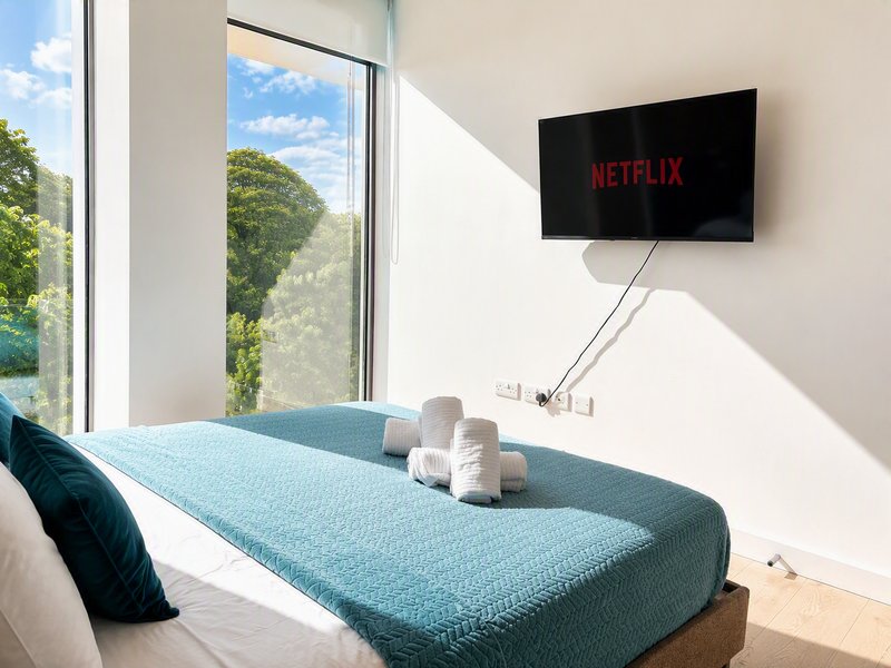 Bright bedroom with double bed, wall-mounted TV, large window overlooking garden
