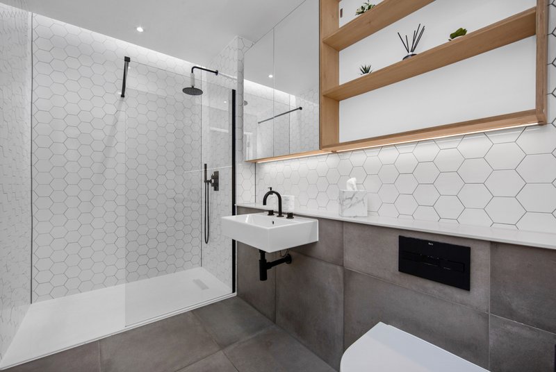 Modern bathroom with walk-in shower, white hexagon tiles, wooden shelving, and grey floor