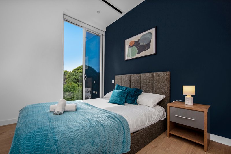 Modern bedroom with double bed, navy wall, wooden nightstand and glass door to garden