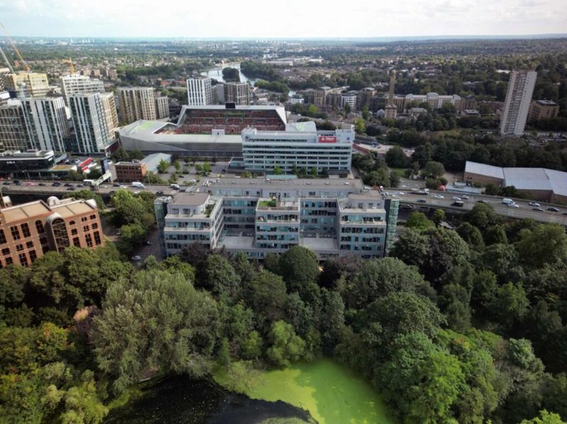 Aerial view of residential apartment buildings surrounded by green trees and water, urban cityscape beyond