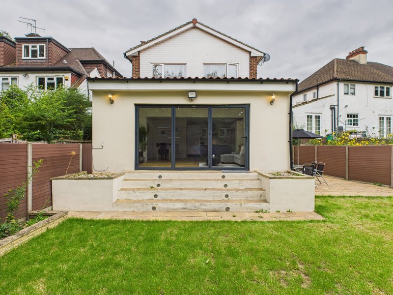 Modern cream-colored house extension with large glass doors, raised deck, and manicured garden