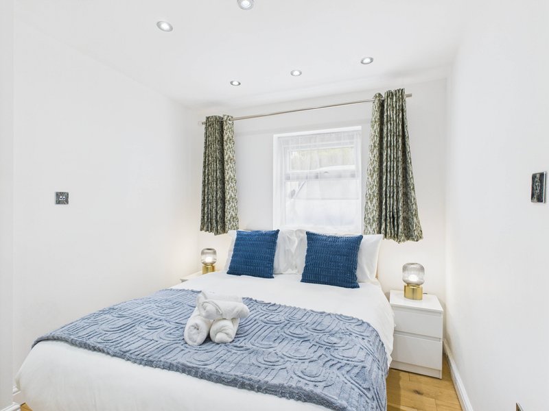 Modern bedroom with double bed, blue pillows, white bedding, and green curtains