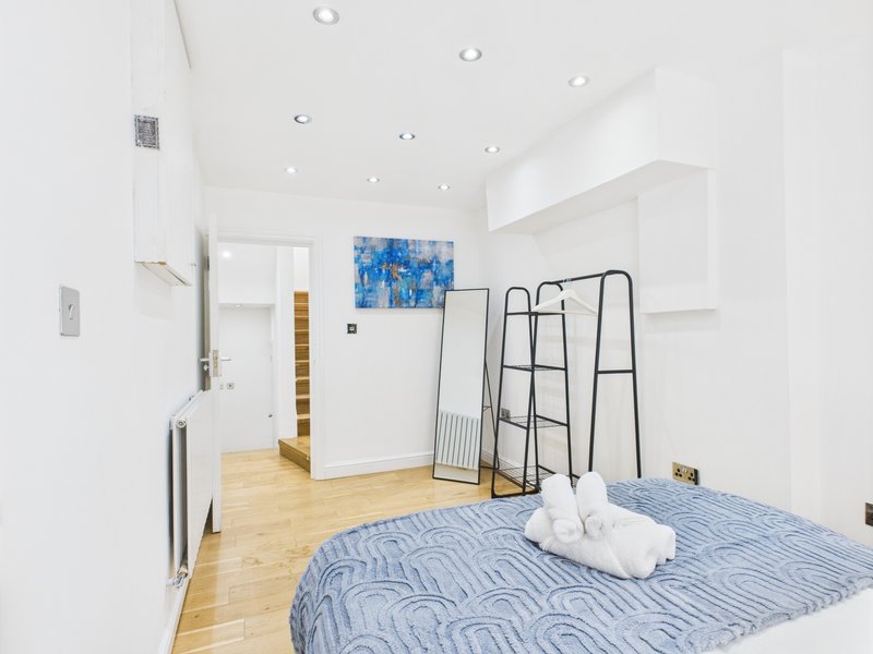 Bright modern bedroom with blue striped bed, wooden floor, white walls and artwork