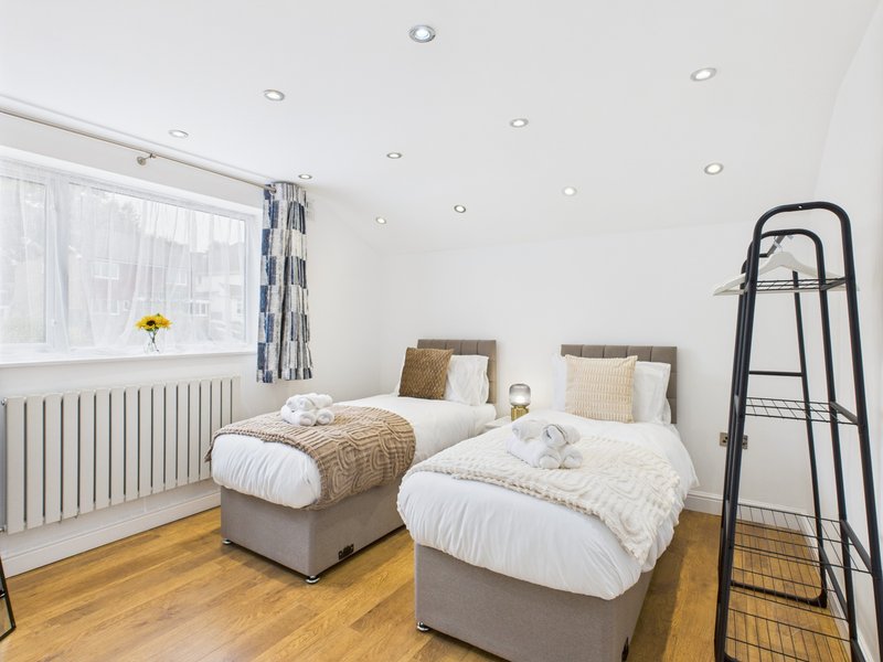 Bright bedroom with two single beds, wooden floor, radiator and window with curtains