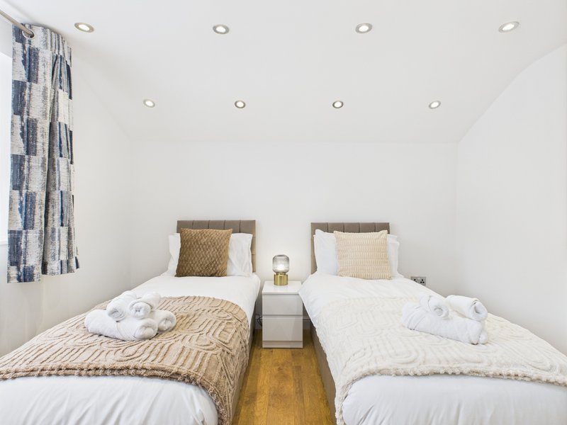 Twin bedroom with two single beds, white bedding, patterned cushions and recessed ceiling lights