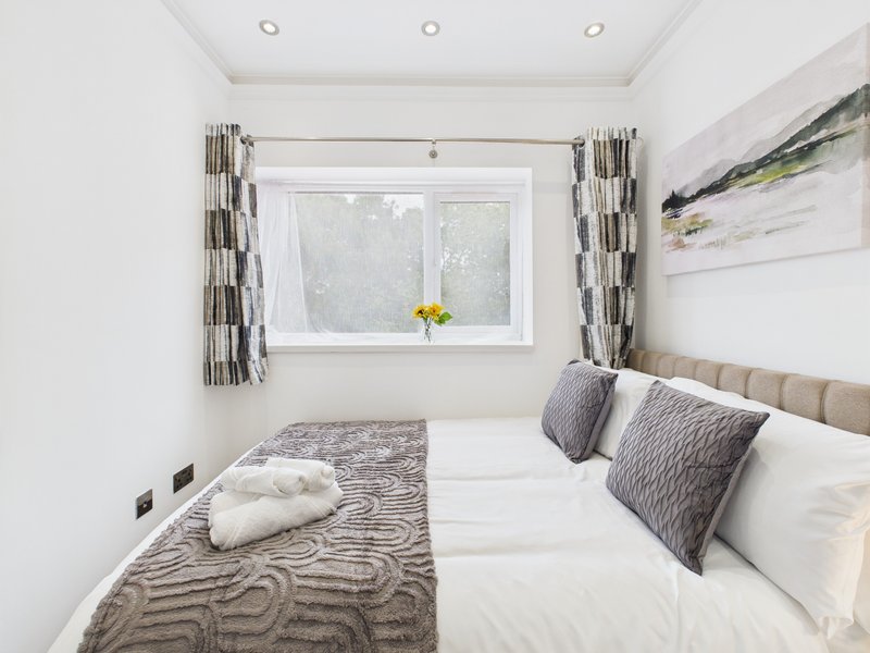 Bright modern bedroom with double bed, patterned bedding, cushions, window with curtains and yellow flowers