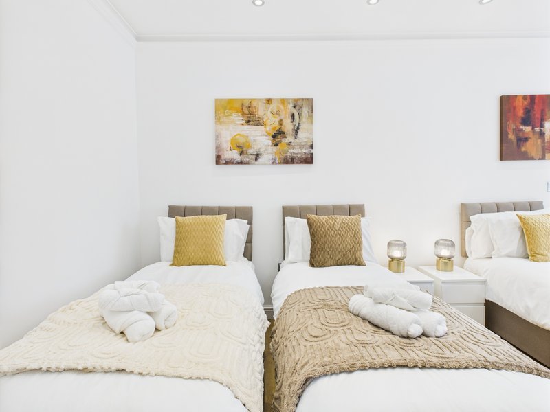 Bright bedroom with two single beds, yellow accent pillows, white bedding and wall art