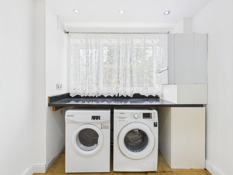 Laundry room with two white washing machines, shelving above, and window with sheer curtains