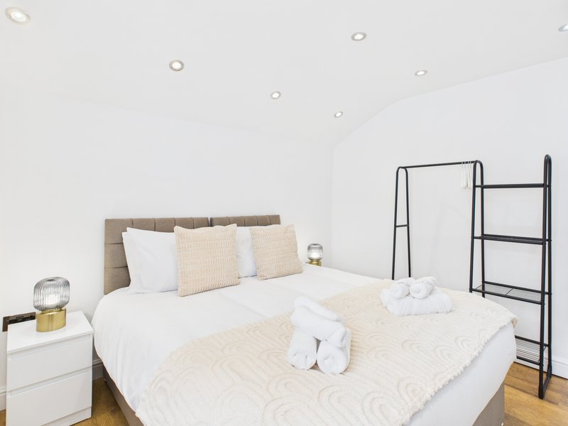 Bright modern bedroom with double bed, cream bedding, upholstered headboard and wooden flooring