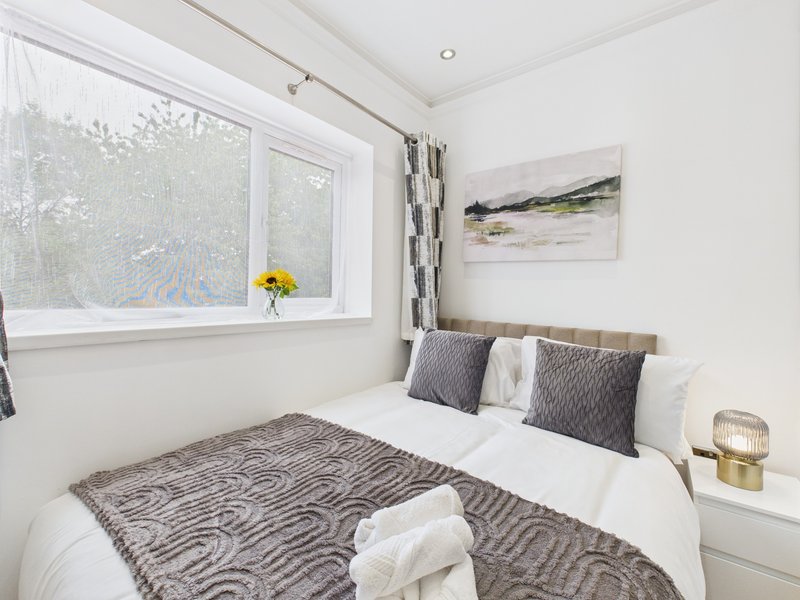 Modern bedroom with double bed, grey patterned bedding, pillows and window with yellow flowers