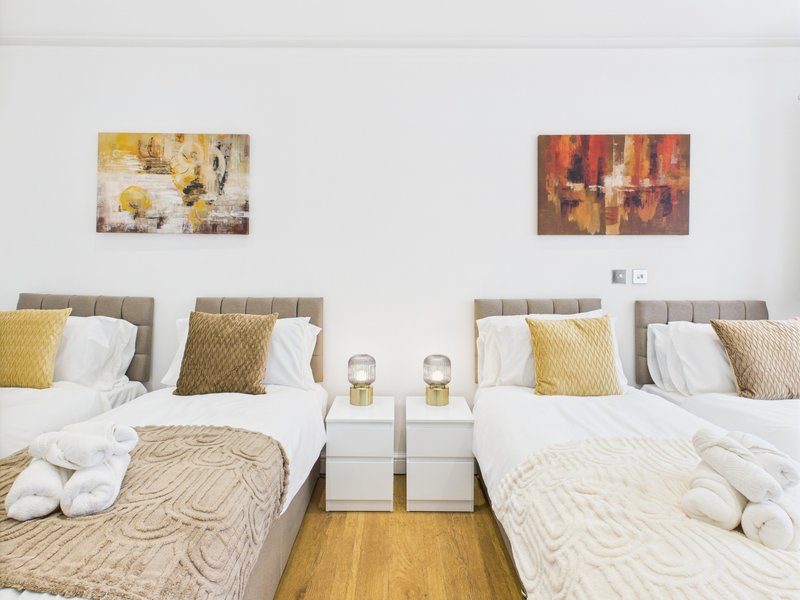 Twin bedroom with two beds, neutral bedding, yellow cushions, wall art and wooden floor