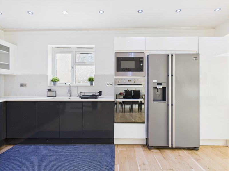 Modern kitchen with black and white cabinetry, stainless steel appliances, and blue floor mat