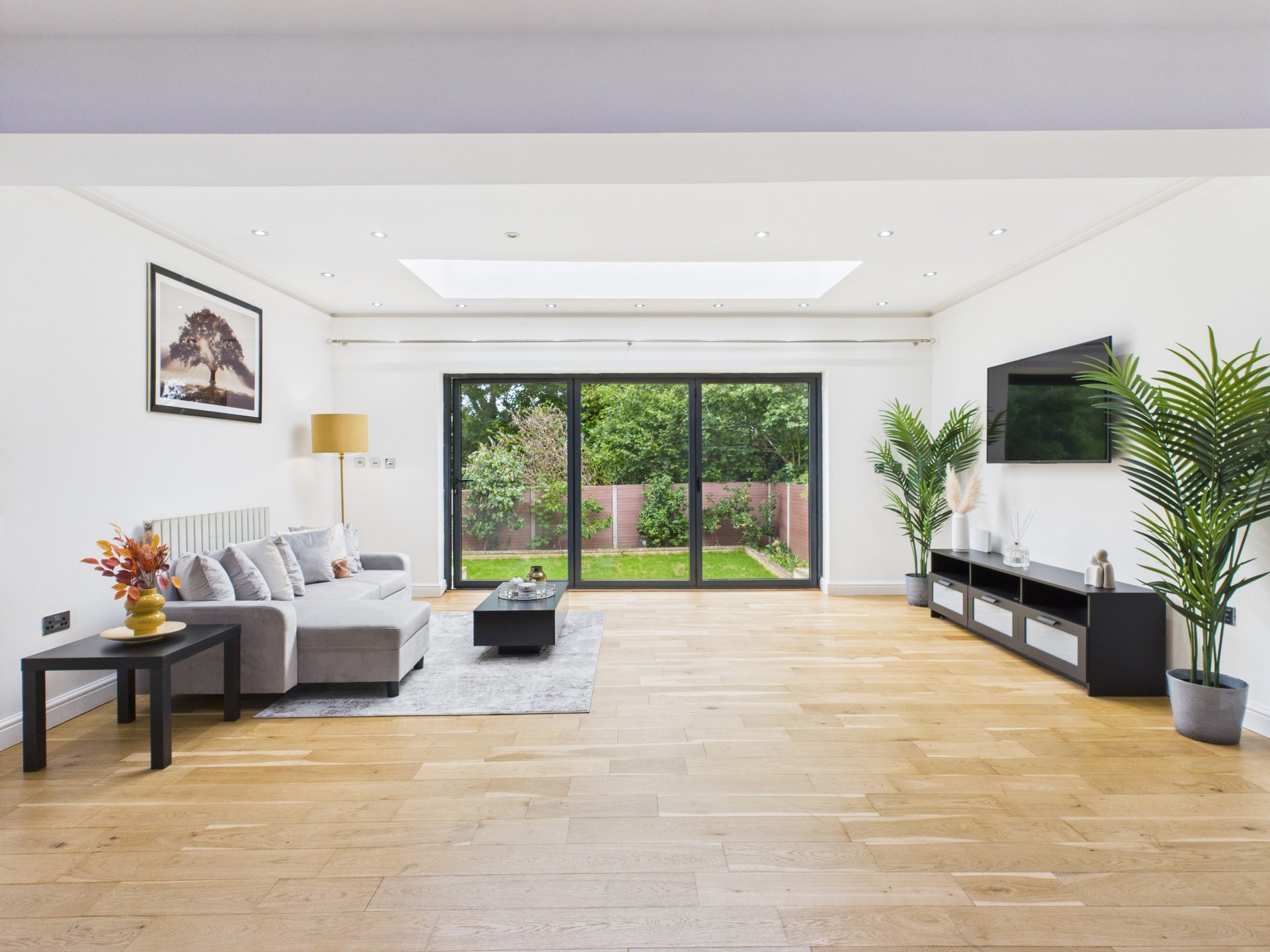Spacious open-plan living room with wooden flooring, grey sofa, large windows and garden view