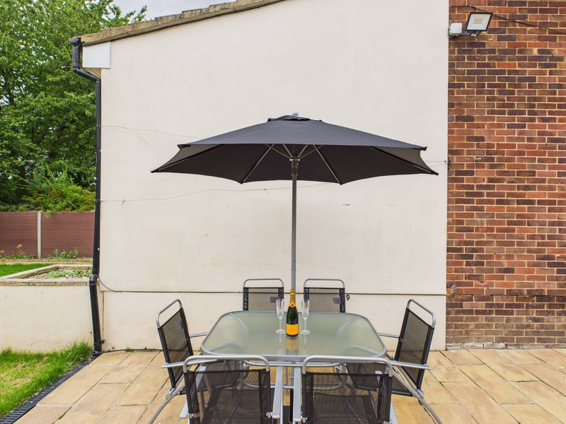 Patio dining set with black umbrella, champagne bottle, and chairs on stone paving