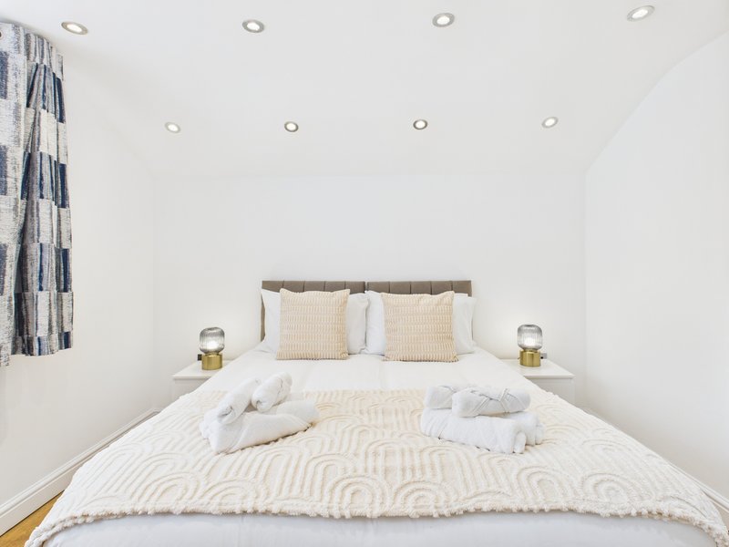 Bright bedroom with double bed, cream bedding, patterned cushions and white towels
