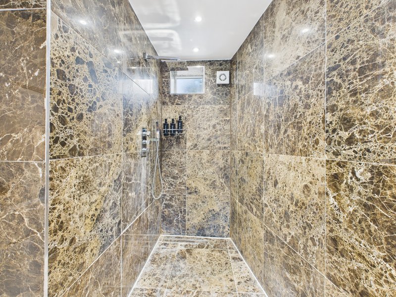 Luxury shower enclosure with marble-effect tiled walls, rainfall showerhead and toiletries shelf