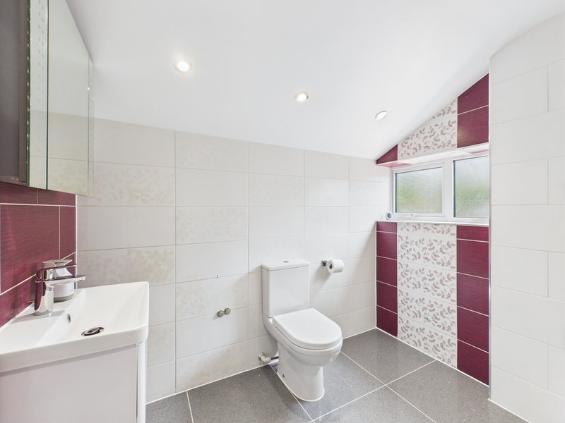 Modern bathroom with white tiles, burgundy accents, sink, toilet and window