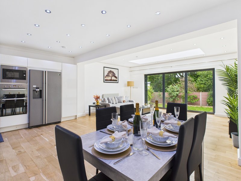 Modern kitchen and dining area with black table, stainless steel appliances, and garden views