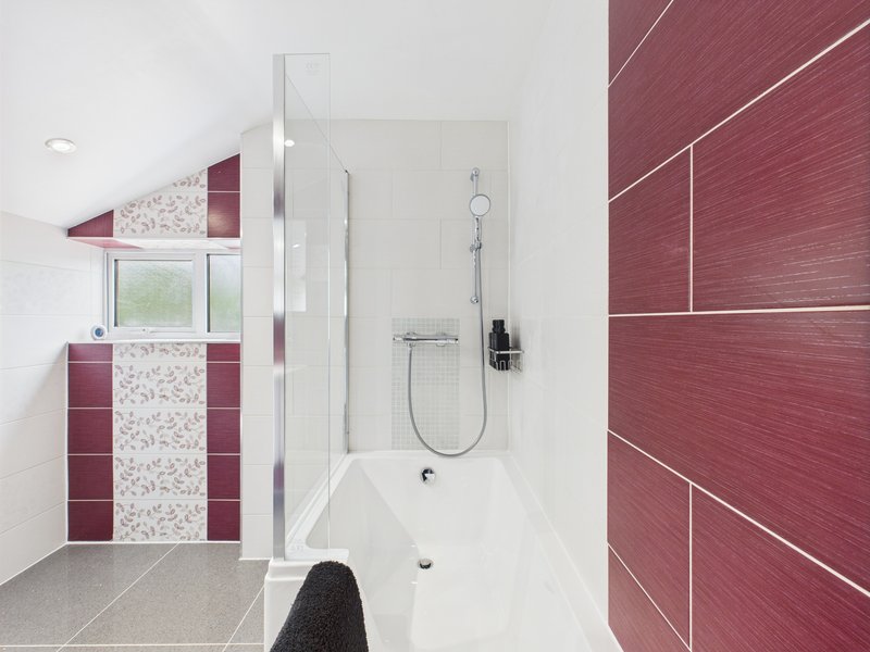 Modern bathroom with burgundy tile walls, walk-in shower enclosure, and pedestal sink