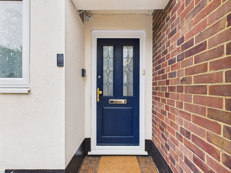 Narrow entrance with navy blue front door, brick wall, white frame and coir doormat