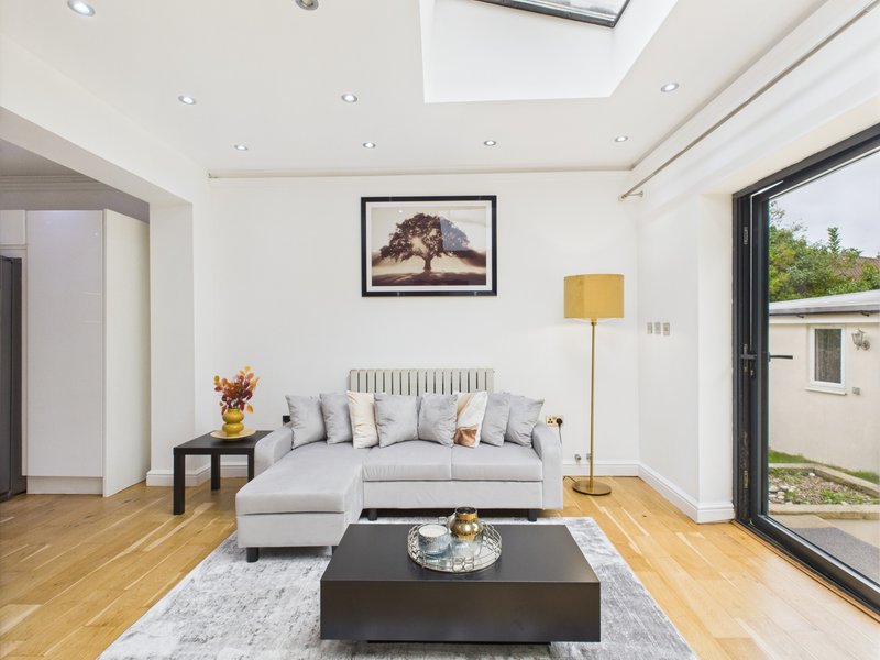Modern living room with light gray sofa, black coffee table, framed wall art, and glass doors to garden