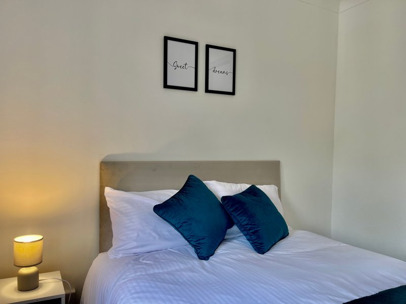 Bedroom with double bed, blue pillows, white bedding, and framed wall art