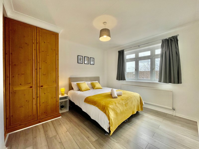 Bright bedroom with double bed, yellow bedding, wooden wardrobe and window with grey curtains