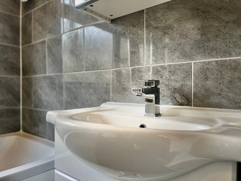 Modern bathroom with dual white sink, chrome mixer tap, grey tile walls and shower enclosure