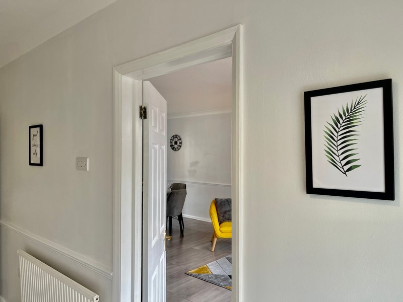 Hallway with open doorway leading to bedroom, featuring framed botanical art and radiator