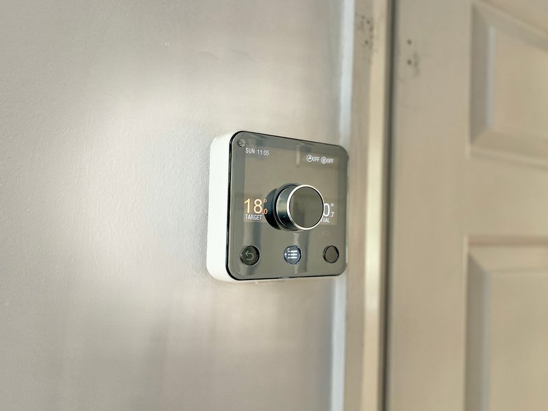 Digital thermostat mounted on white wall showing temperature reading