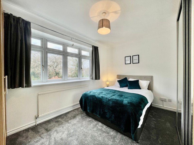Bright bedroom with double bed, teal velvet throw, large window with black curtains and ceiling light