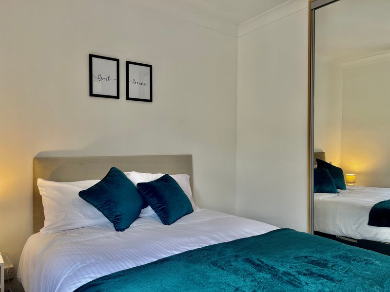 Modern bedroom with double bed, white bedding, teal throw, and mirrored wardrobe