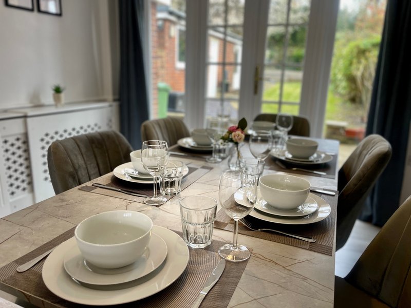 Dining room with wooden table set for meal, upholstered chairs, garden view through large windows