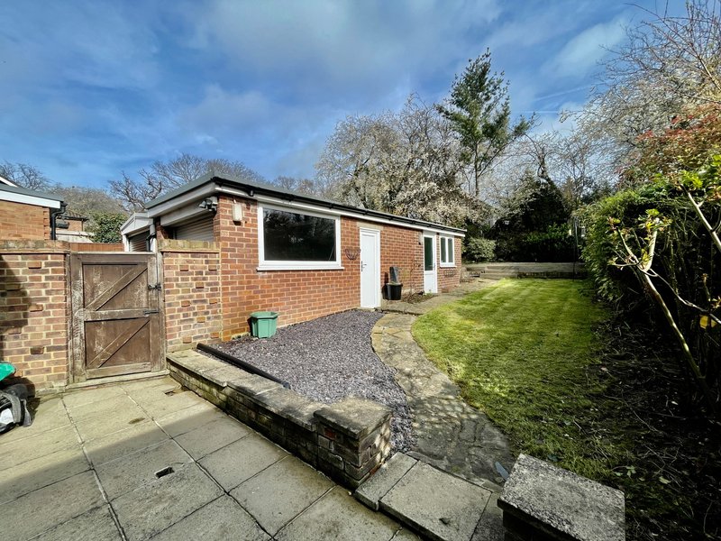Modern brick bungalow with driveway, garden, and mature trees surrounding property