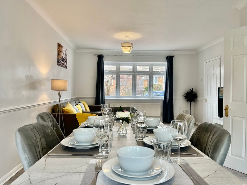 Bright dining room with marble table, place settings, gray upholstered chairs and black curtains