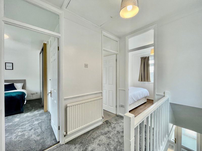 Bright hallway with white doors, radiator, pendant light and staircase railing