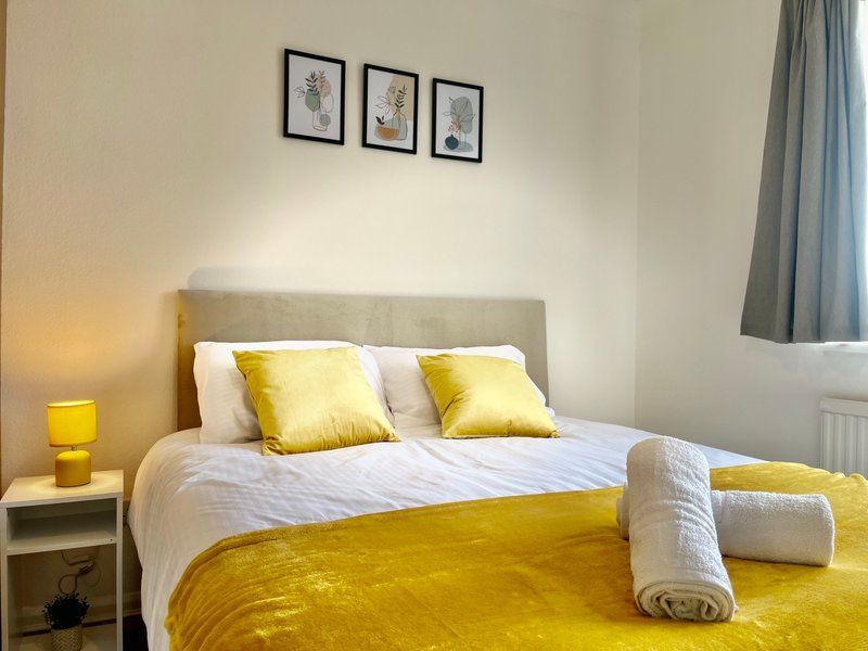 Bedroom with double bed, yellow bedding, white pillows, grey headboard and framed wall art