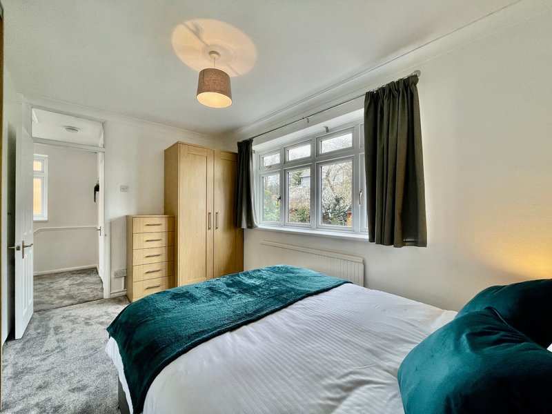 Bright bedroom with double bed, teal bedding, wooden wardrobe and window with view