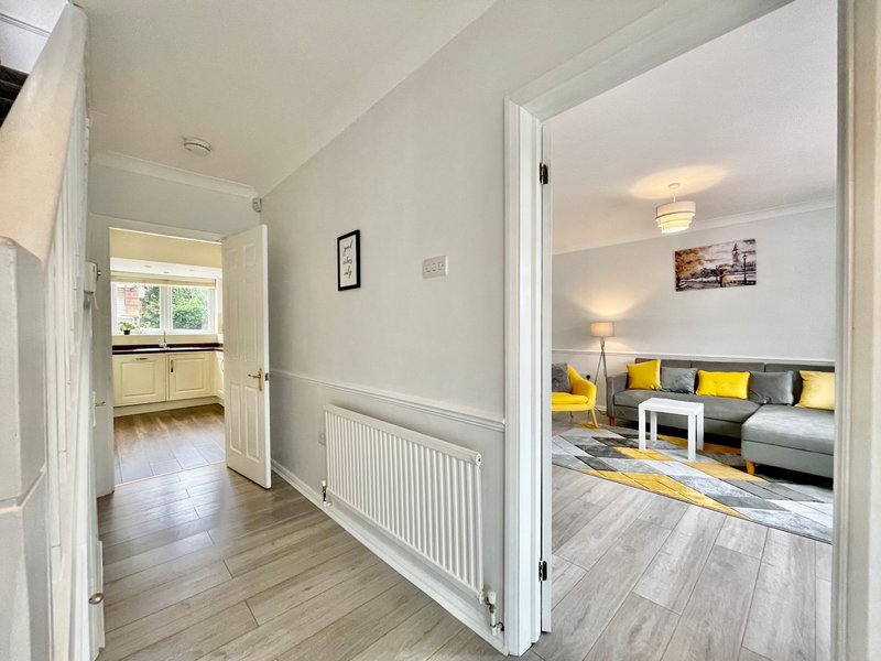 Bright hallway with white walls, wooden flooring, and open doors to adjacent rooms