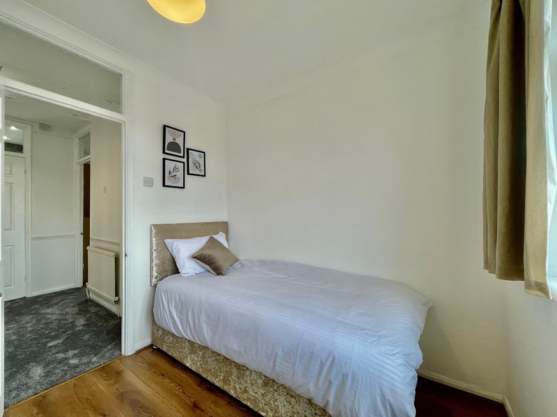 Bright bedroom with single bed, wooden headboard, white bedding, framed wall art, and olive curtains