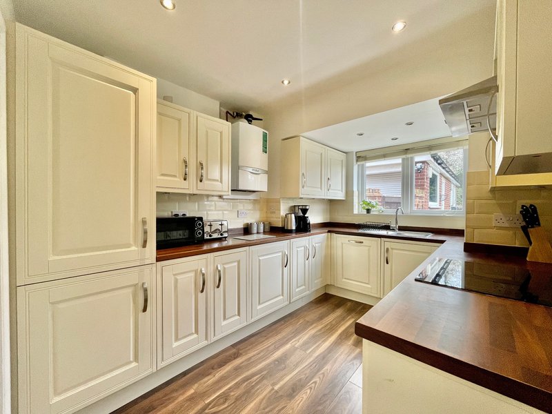 Modern cream kitchen with white cabinetry, dark worktops, wooden flooring and window view
