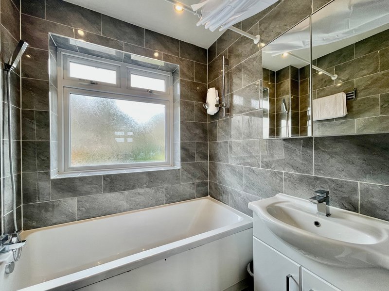 Modern bathroom with grey tile walls, white bathtub, sink vanity and window