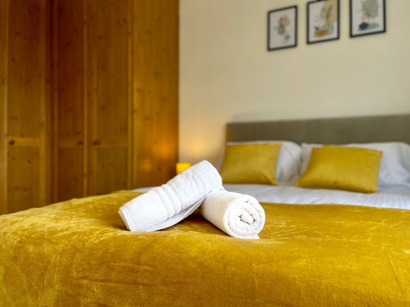 Bedroom with yellow bedding, rolled white towels, yellow cushions and wooden wardrobe