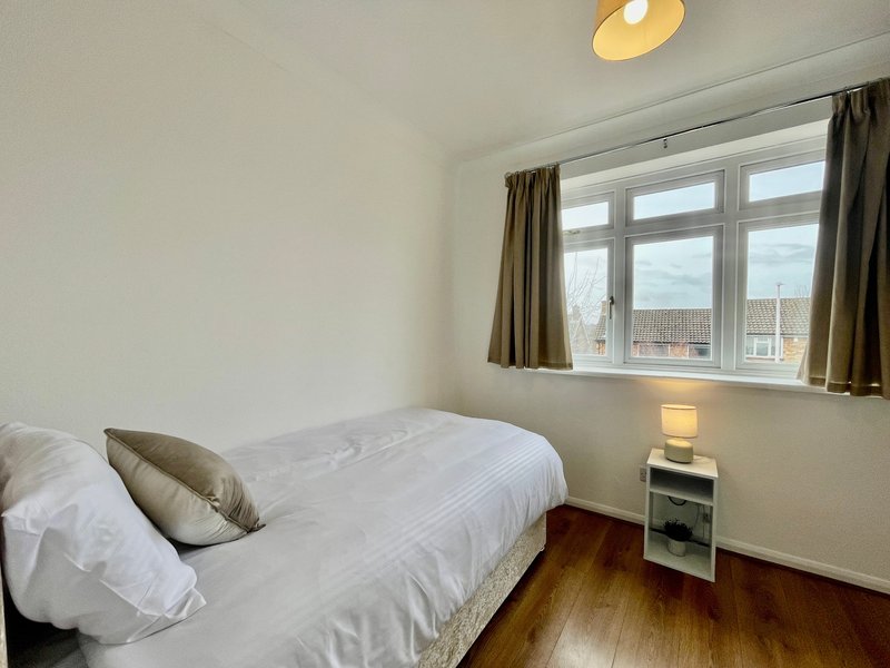 Bright bedroom with single bed, white bedding, wooden floor and large window with city views