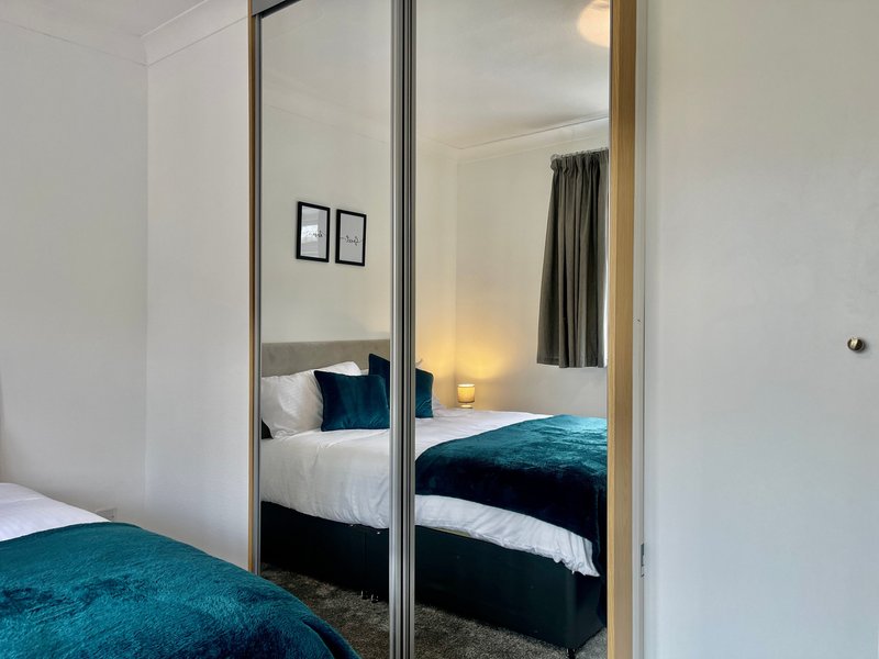 Modern bedroom with double bed, mirrored wardrobe doors and teal bedding