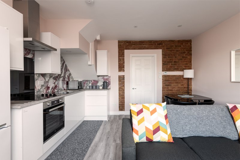 Open-plan kitchen and living area with white cabinetry, brick accent wall, grey sofa with patterned cushions